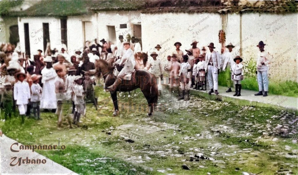 Carnavales de la Guarenas de antaño en la calle Régulo Fránquiz, frente a la Plaza Bolívar, década de 1920. Al fondo, esquina de la calle Bolívar. Fotografía restaurada y coloreada digitalmente por Campanario Urbano.